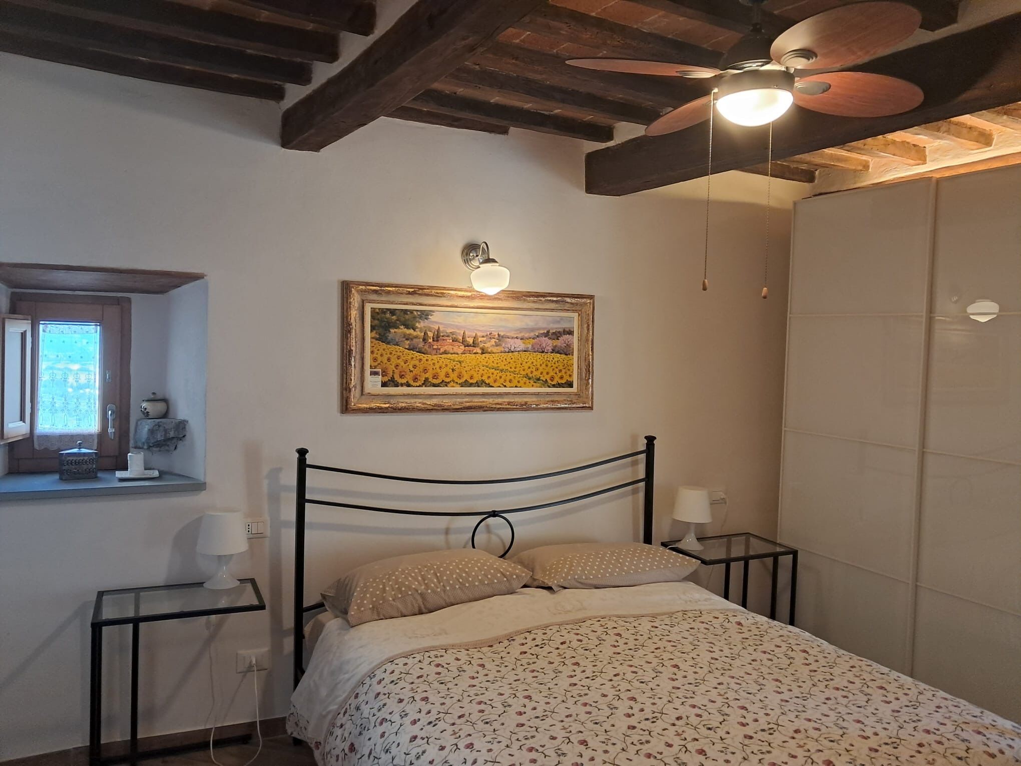 Ein Schlafzimmer mit Bett, Deckenventilator, einem Gemälde, einem Fenster und einem Nachttisch.