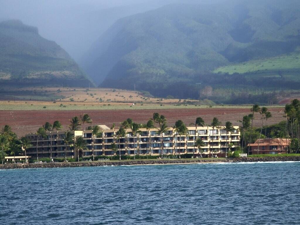 A beachfront hotel with multiple balconies, a pool, and a view of the ocean and mountains.