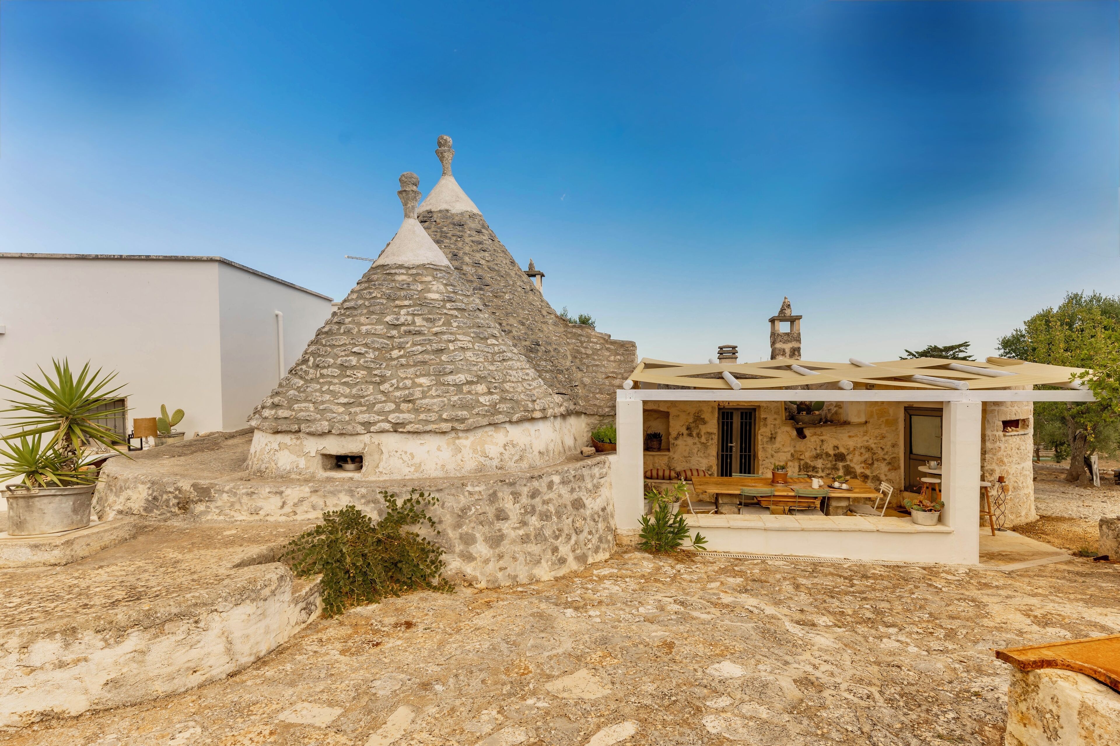 A stone house with a conical roof, a small balcony, and a covered outdoor seating area.