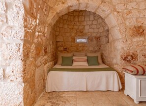 A room with a stone wall, a bed with a green pillow, and a small window.