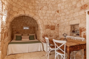 A stone-walled room with a bed, a wooden table, and chairs. -  Trullo Happy Sunrise (ostuni)