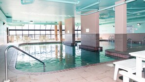 Una piscina interior amb aigua cristal·lina, parets de rajola i una zona al costat de la piscina amb cadires i una taula.
