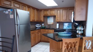 Una cuina amb armaris de fusta, un refrigerador d'acer inoxidable, un taulell negre i una zona de menjador amb caires de fusta.