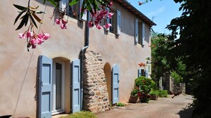 Un edificio in pietra rustica con facciata tradizionale, vialetto sterrato e vegetazione rigogliosa.