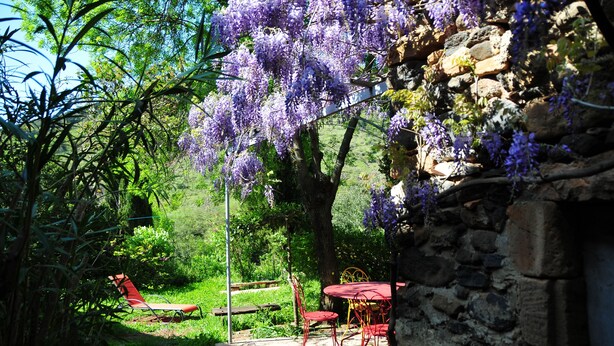 Un giardino con un muro di pietra, una panchina di legno e un tavolo con sedie.