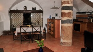 Zona pranzo con tavolo e sedie, un vaso con fiori, e angolo cottura con televisore e pensili.