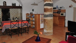 Zona pranzo con tavolo apparecchiato per due, una libreria in legno e angolo cottura con forno a microonde e frigorifero.
