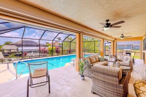 Zona junto a la piscina con mobiliario de mimbre, ventilador de techo y vista a la piscina y al paisaje circundante.