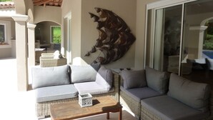 Una veranda luminosa con un divano in vimini, un tavolo in legno e un elemento decorativo a parete.