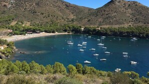 A coastal area with boats on a calm sea, surrounded by hills and sparse vegetation.