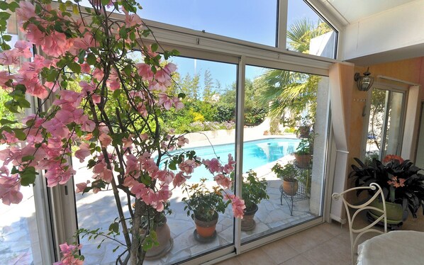Una habitación con amplias puertas de cristal que dan a una zona de piscina, plantas en macetas y una silla.