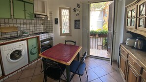 A compact kitchen with a washing machine, a table with chairs, and a window with a view of the outside.