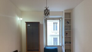 A bedroom with two beds, a wardrobe, a chair, a bookshelf, and a window with a view.