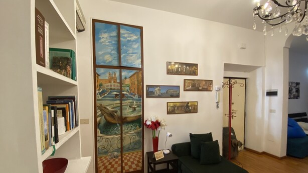 A living room with a bookshelf, a sofa, a painting, and a chandelier.