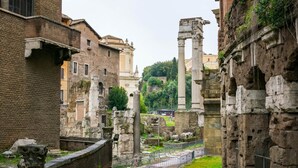 An ancient Roman site with ruins, including columns and stone structures, surrounded by modern buildings.