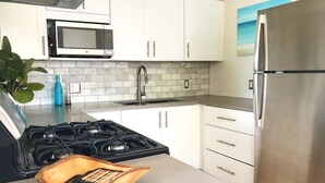 A modern kitchen with white cabinets, a stainless steel refrigerator, a gas stove, a microwave, and a sink. - Clearview Villas (LOWER): Casual, Bright, Steps from Sea, Great for families! (Island Harbour)