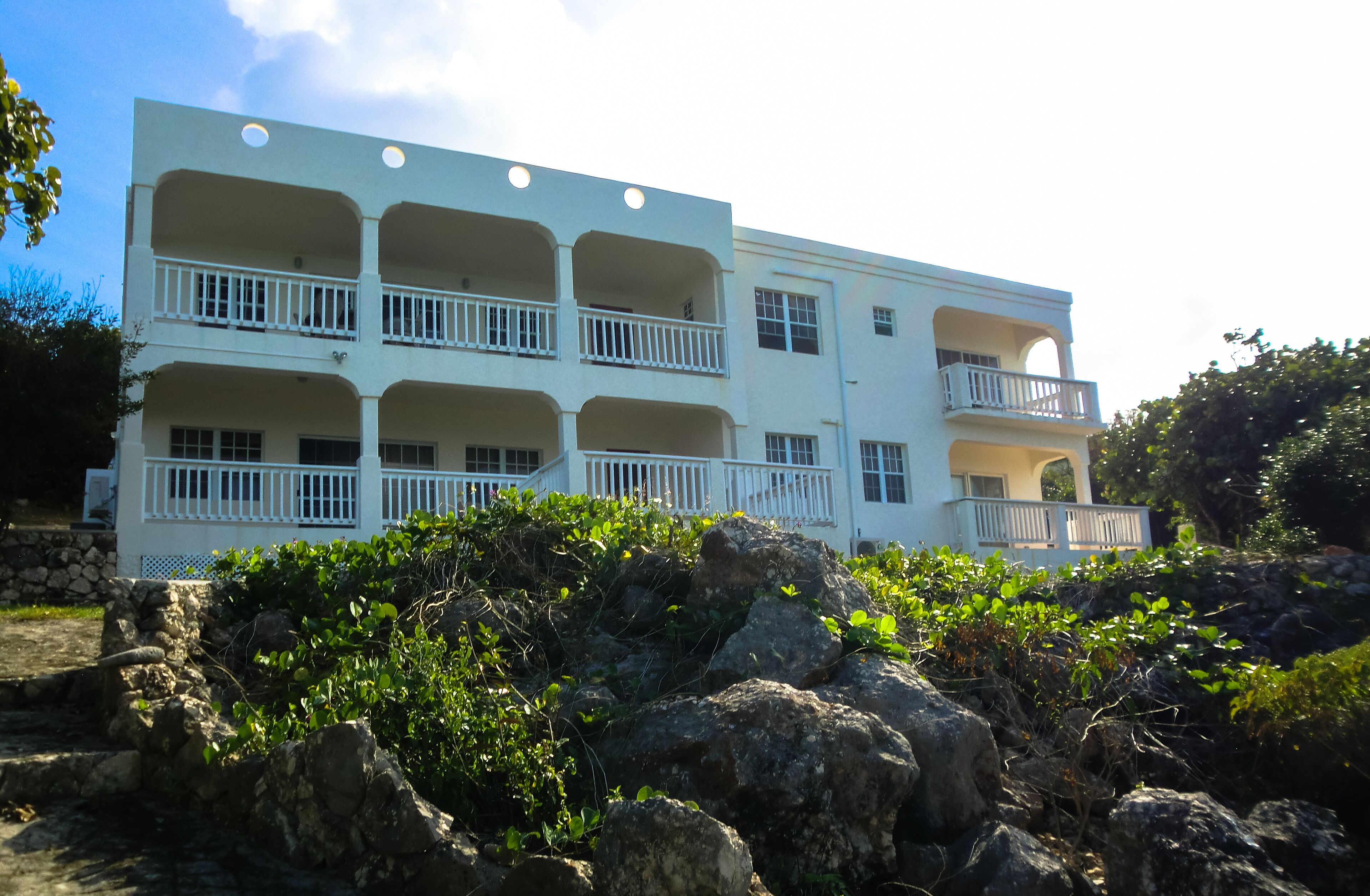 A multi-story building with balconies, surrounded by rocks and greenery.