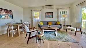 A living room with a sofa, chairs, a coffee table, and a dining area with a table and chairs. - Clearview Villas (LOWER): Casual, Bright, Steps from Sea, Great for families! (Island Harbour)