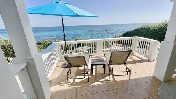 A covered patio with two chairs and a table, overlooking the sea. - Clearview Villas (LOWER): Casual, Bright, Steps from Sea, Great for families! (Island Harbour)