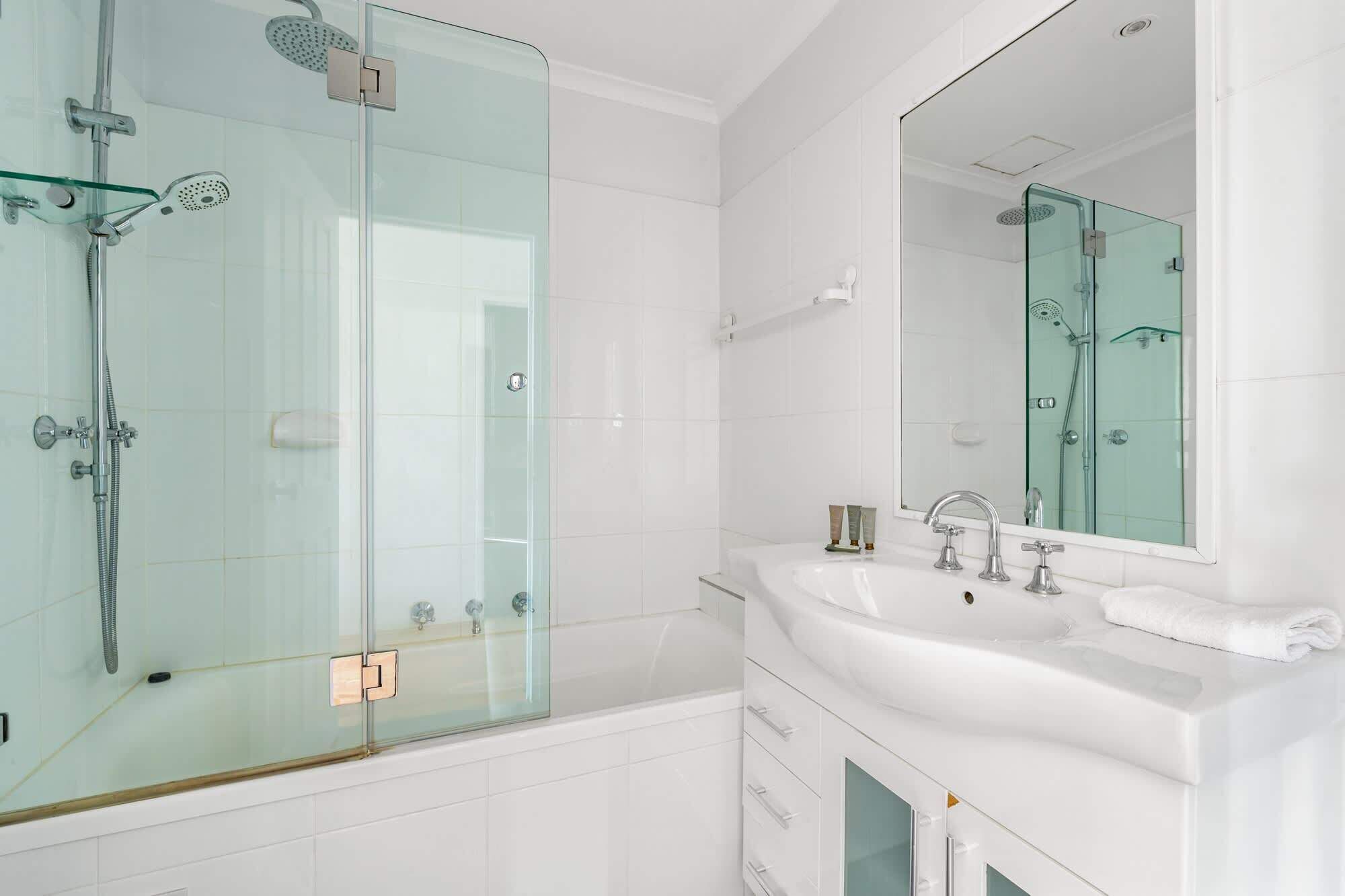 Un baño moderno con ducha de vidrio, lavamanos blanco y un espejo grande.