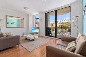 A modern living room with a large window, a flat-screen TV, and a balcony with outdoor furniture.