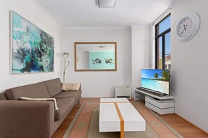 A living room with a sofa, a coffee table, a TV, a painting, a mirror, and a clock.