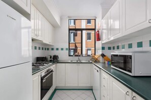 A compact kitchen with white cabinets, a gas stove, a microwave, and a window overlooking a brick building.