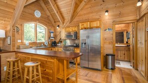 Cocina rústica de cabaña con una isla central, taburetes de bar, un refrigerador de acero inoxidable y un microondas.