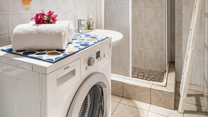 Un baño moderno con lavadora integrada, un lavabo con toalla y un box de ducha de vidrio.