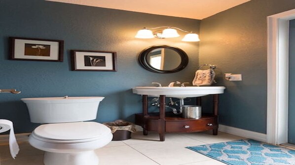 A bathroom with a toilet, a sink, and a mirror. There are framed pictures on the wall and a rug on the floor.