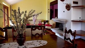 A dining area with a wooden table, chairs, and a vase of flowers. There is a fireplace with a mantel and a wall-mounted lamp.