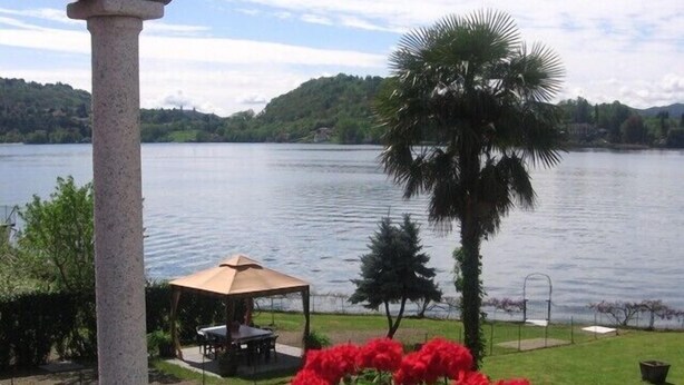 A lakeside view with a gazebo, a palm tree, and a flower bed.