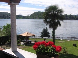 A lakeside view with a gazebo, a palm tree, and a flower bed.