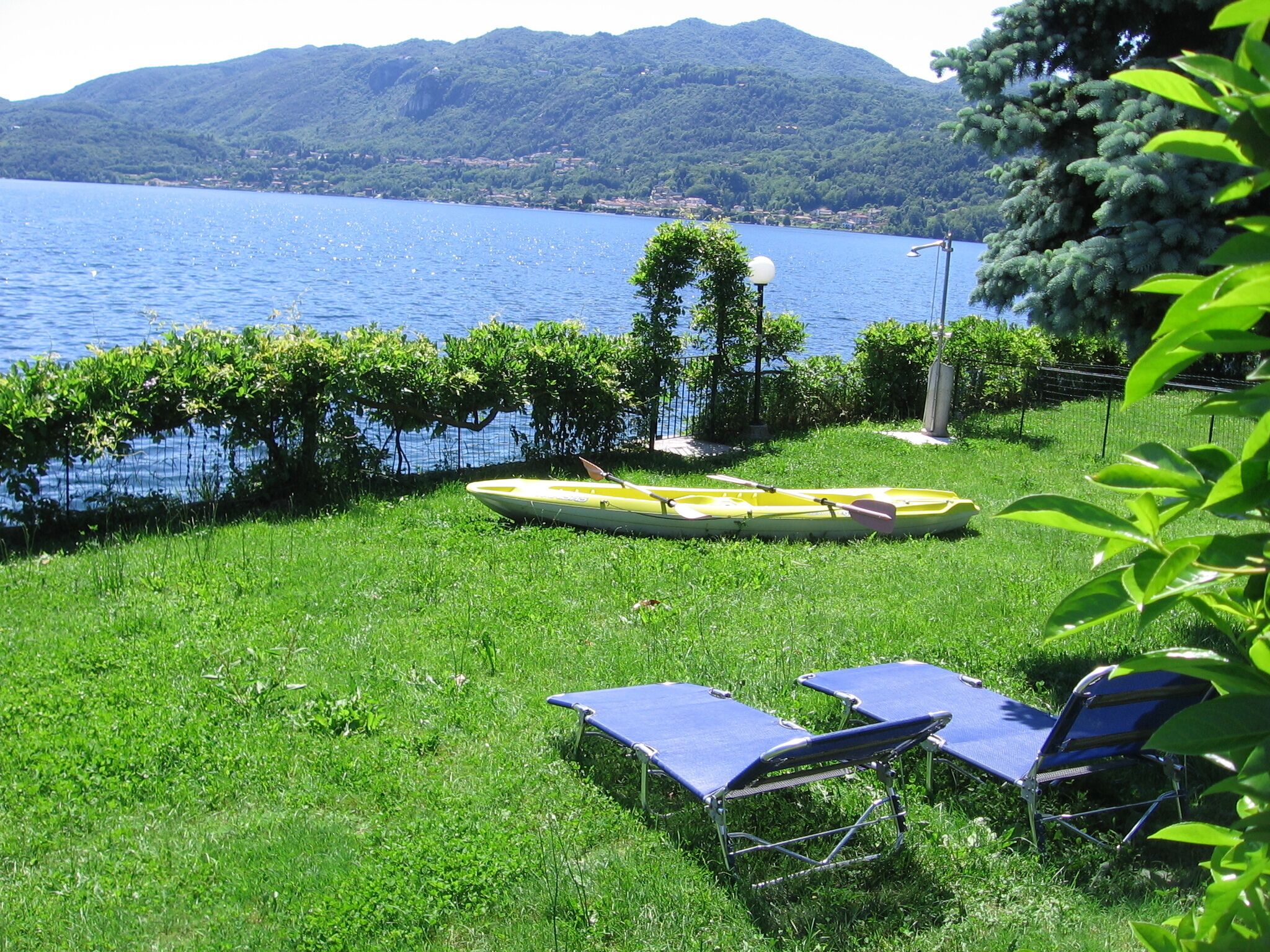 Une zone herbeuse avec une rangée de chaises longues bleues, un kayak jaune et un lampadaire.