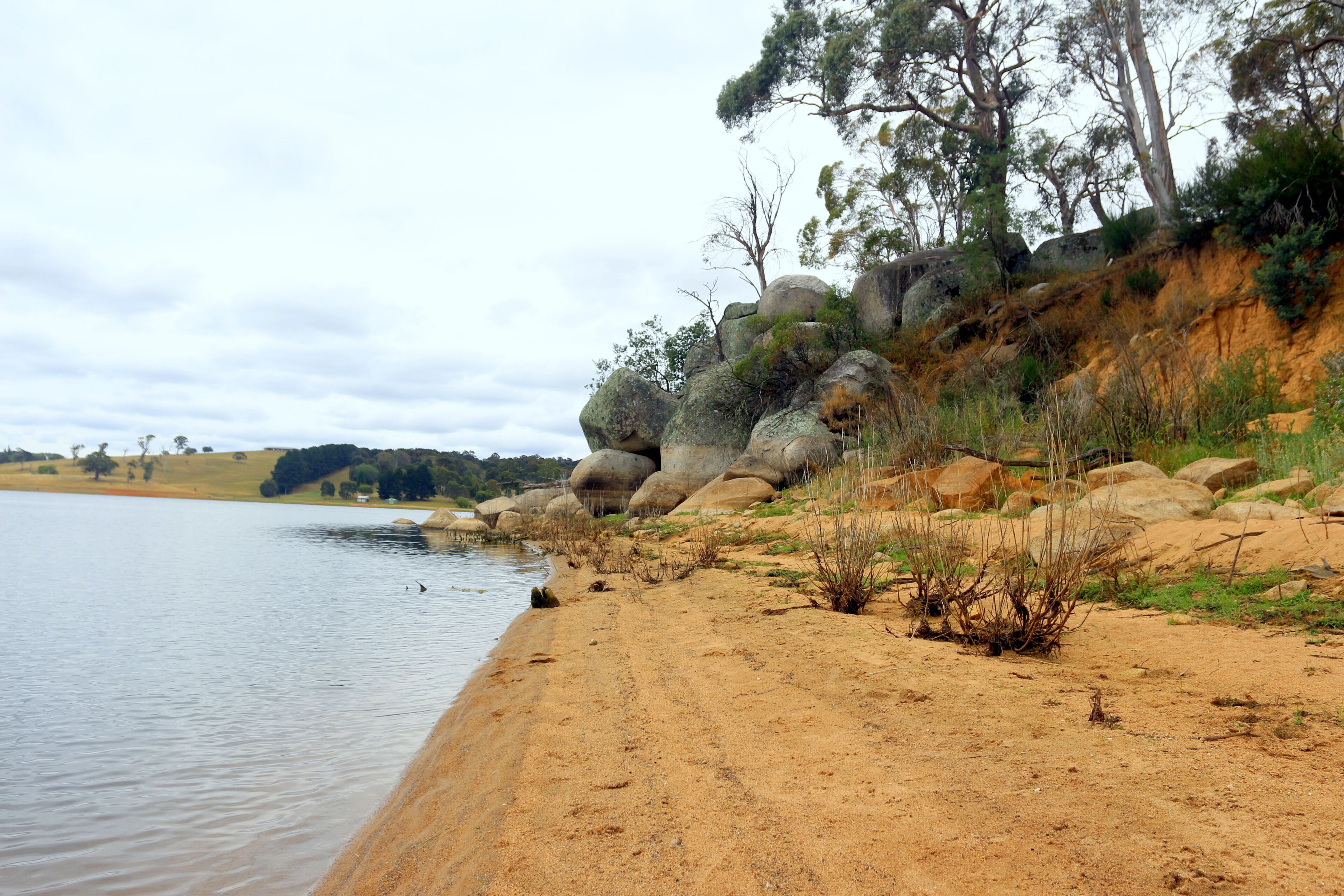 Ein sandiger Strand mit großen Felsen und vereinzelter Vegetation.