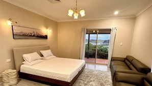 A bedroom with a bed, a sofa, a chandelier, a painting, and a view through a glass door. - Luxury 5BR Lakefront Homestead — 55 Acres, Sandy Beach, Firepit (Oberon)