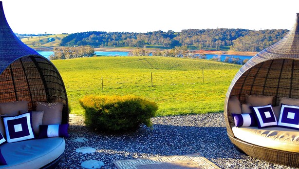Two outdoor seating areas with cushions and a view of a green field and water body. - Luxury 5BR Lakefront Homestead — 55 Acres, Sandy Beach, Firepit (Oberon)