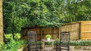 An outdoor seating area with two chairs and a table, surrounded by a wooden fence and lush greenery.
