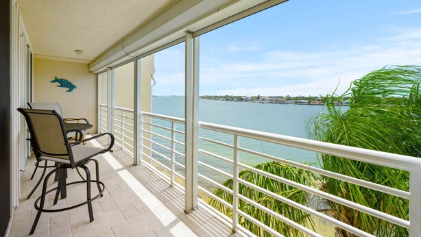 A balcony with a table and chairs, overlooking a body of water and a distant shoreline.