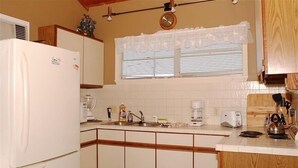 Una cocina con refrigerador, cafetera y ventana con persianas.