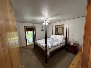 A bedroom with a four-poster bed, a ceiling fan, a wooden nightstand, and a mirror.