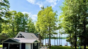 Un chalet au bord du lac, doté d’un garage, entouré d’arbres et offrant une vue dégagée sur le lac.