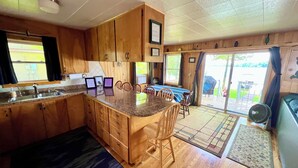 Une cuisine avec des meubles en bois, un plan de travail en granit, un coin repas avec une table et des chaises, et une vue à travers la porte vitrée.