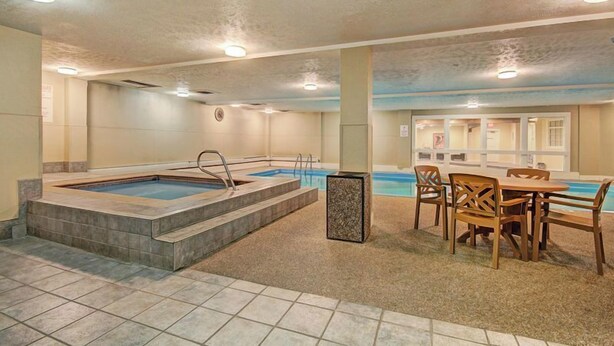 Uma piscina com área de estar e mesa, cercada por paredes e teto com iluminação embutida.
