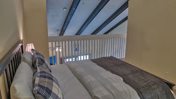 A bedroom with a sloped ceiling, a bed with multiple pillows, and a view of the balcony.