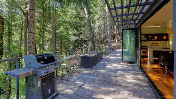 A wooden deck with a grill, outdoor seating, and a glass-enclosed bar area.