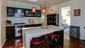 A modern kitchen with dark cabinets, a central island with two red chairs, and pendant lighting.