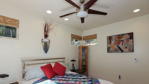A bedroom with a bed, a ceiling fan, a bookshelf, and a painting on the wall.
