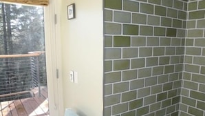 A room with a glass door leading to a balcony, a tiled shower wall, and a small framed picture on the wall.
