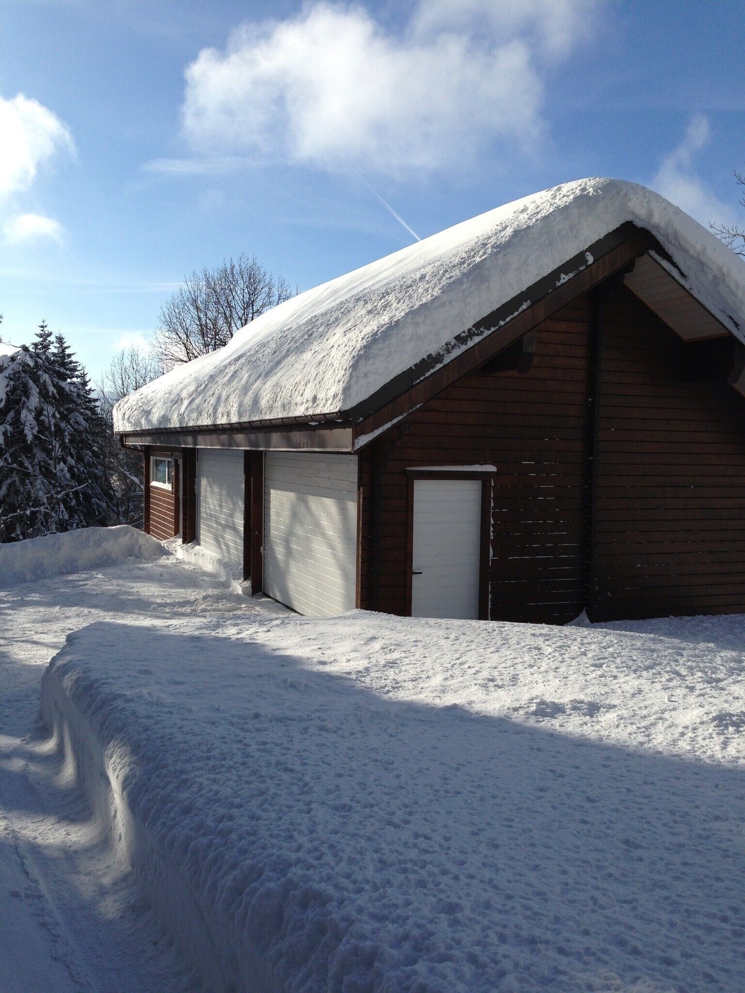 Una baita di legno con tetto imbiancato dalla neve e un'autorimessa, immersa nella neve.